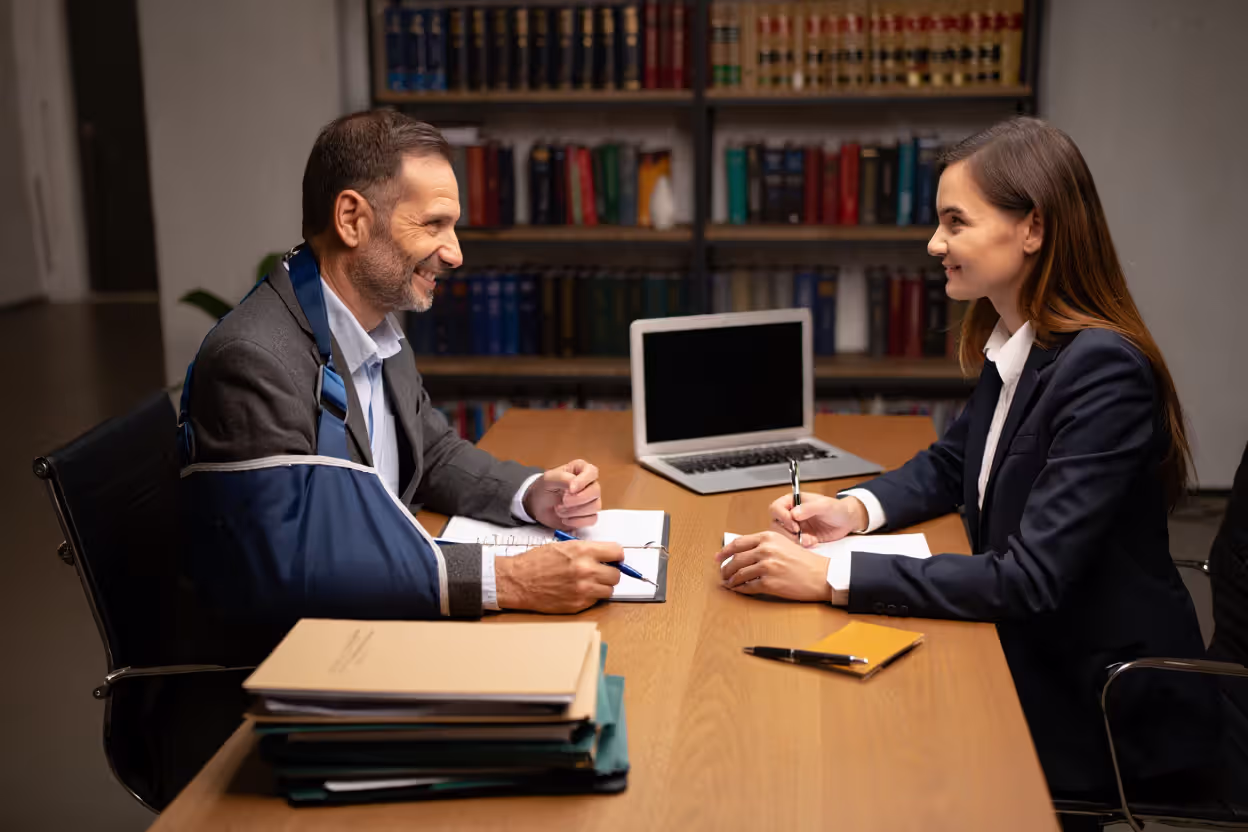 Injured client with a bandaged arm consulting a truck accident attorney in a modern law office with legal documents and laptop on the desk